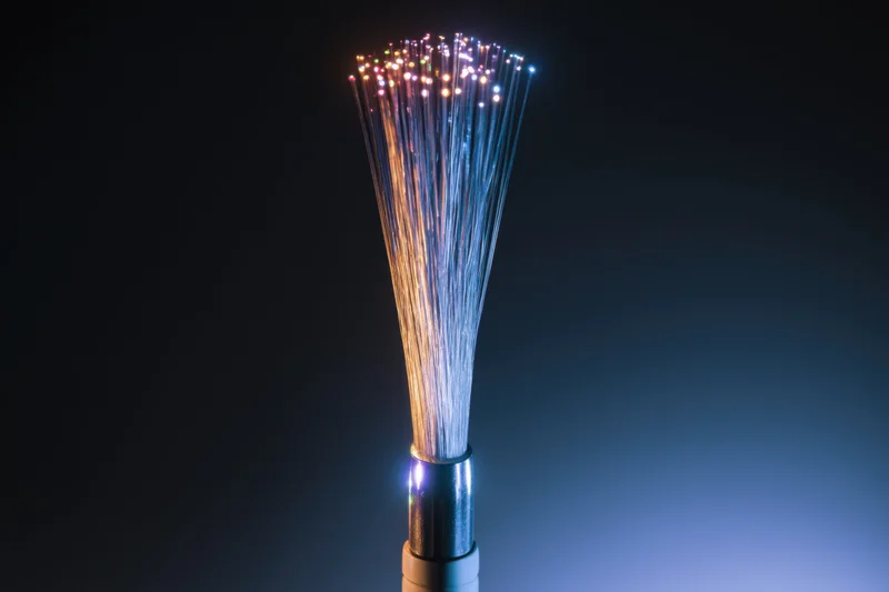 Close-up of fiber optic cable with glowing multicolored strands fanning out from connector against dark background