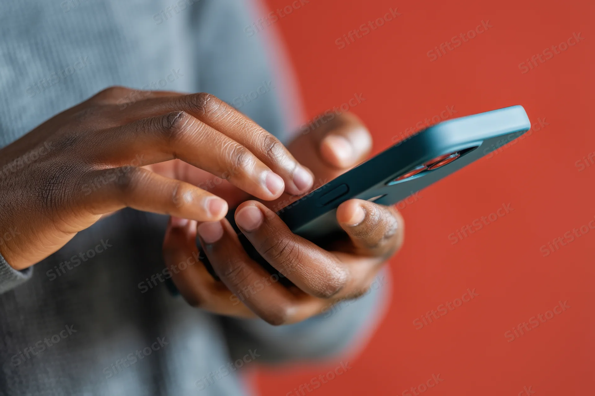 Close-up of hands interacting with a smartphone against a red background