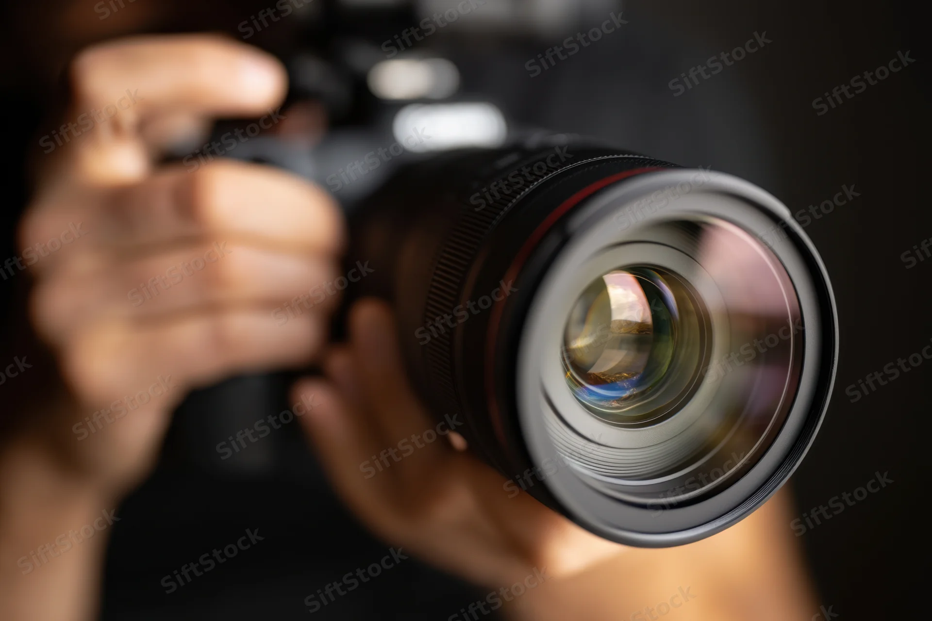 Close-up of a professional DSLR camera lens being held in hand with visible reflection in glass