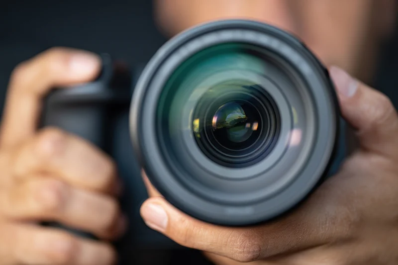 Close-up of a professional DSLR camera lens held in hands with visible reflection in glass