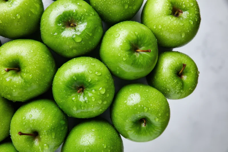 Cluster of shiny green apples with water droplets on marble surface