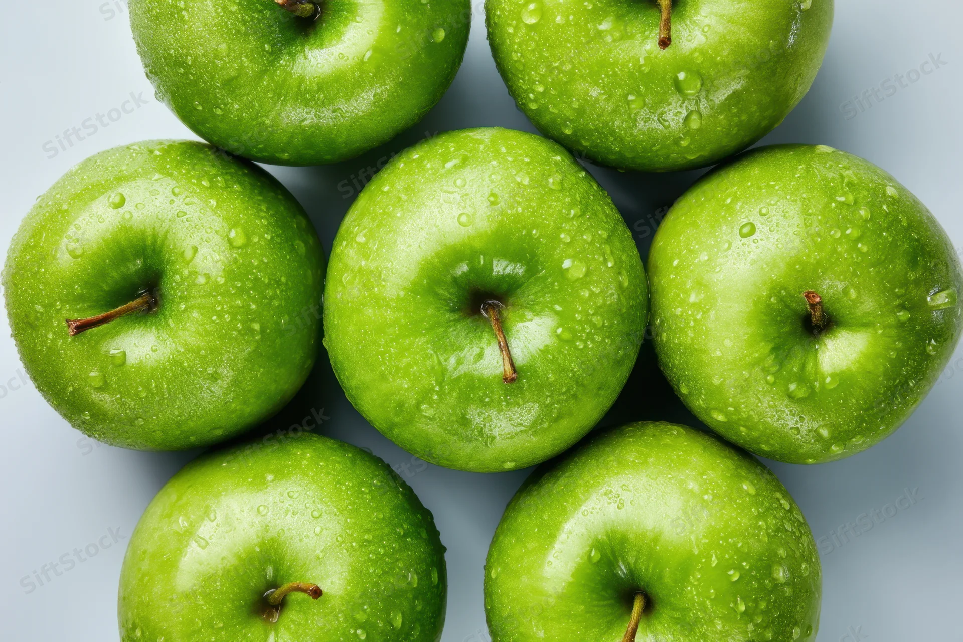 Cluster of shiny green apples with water droplets arranged on a white surface