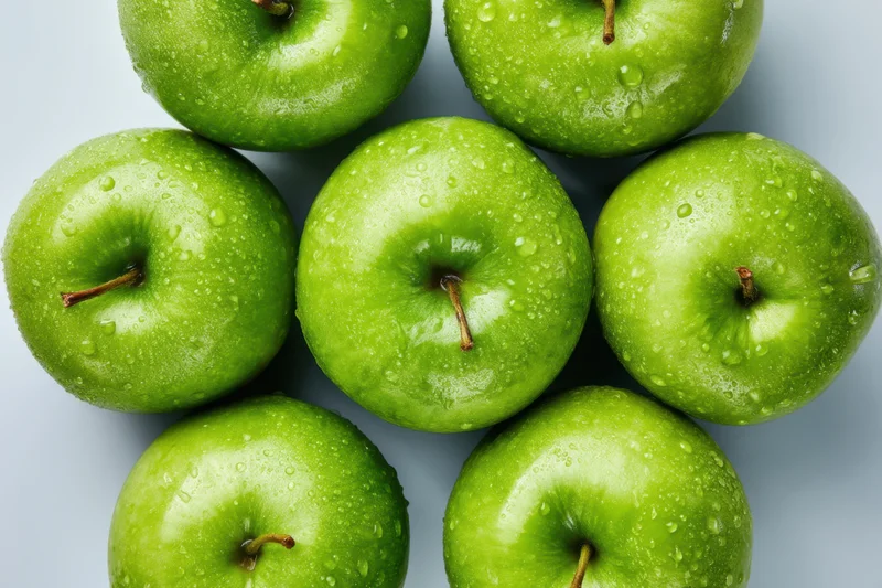 Cluster of shiny green apples with water droplets arranged on a white surface
