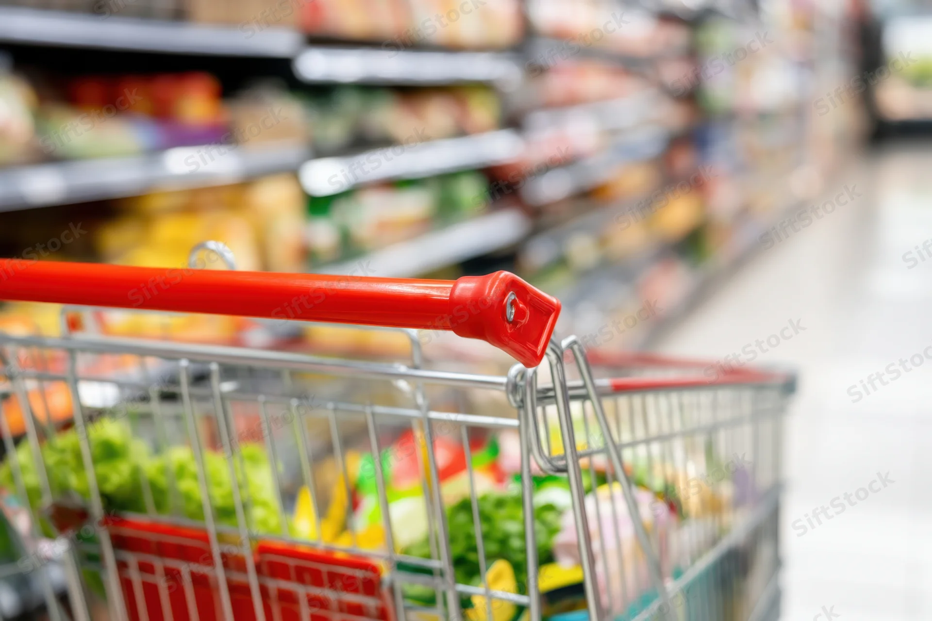 Metal shopping cart filled with fresh vegetables in a supermarket aisle