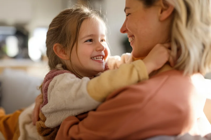 Mother and daughter hugging and smiling indoors on a sofa