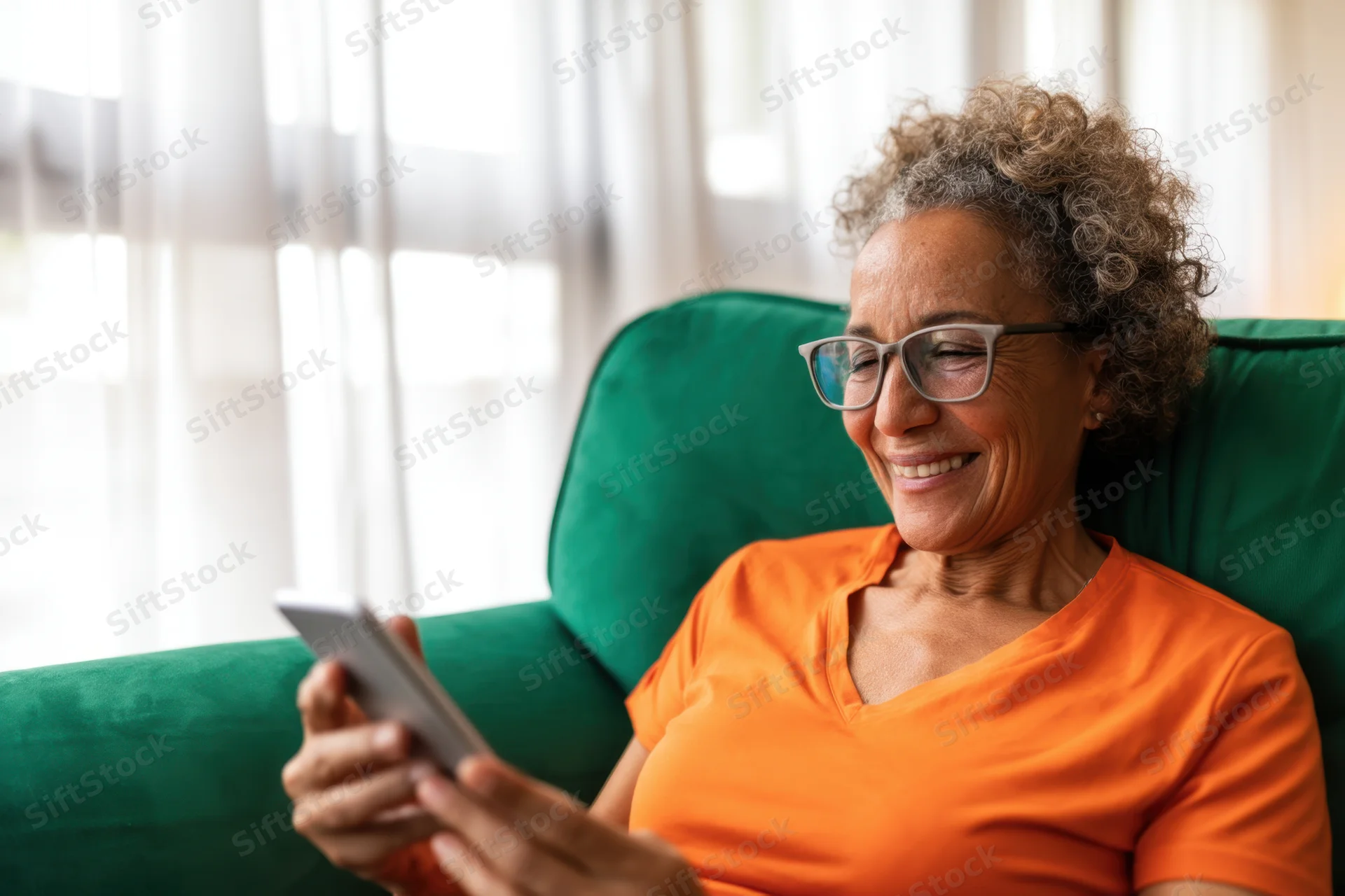 Senior woman smiling while using smartphone on green couch in living room