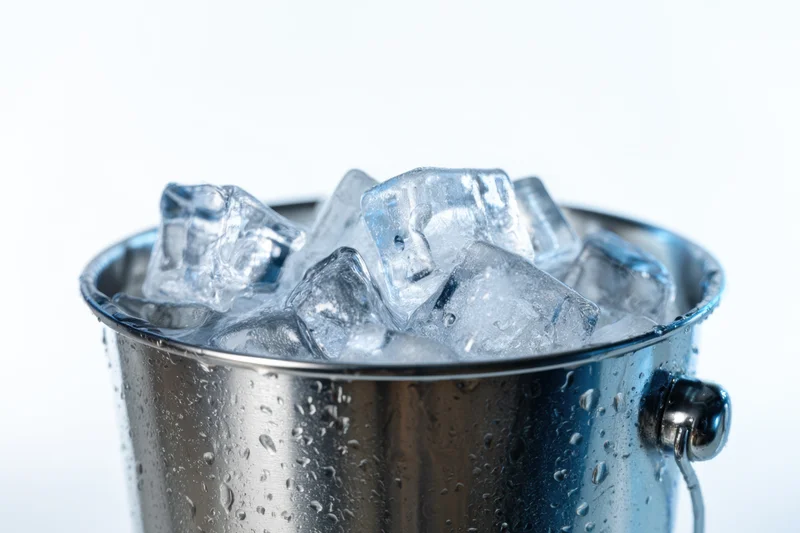 Stainless steel bucket filled with clear ice cubes, condensation on surface, isolated on white background
