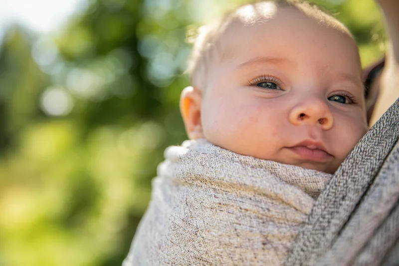 Baby wrapped in a textured fabric sling outdoors