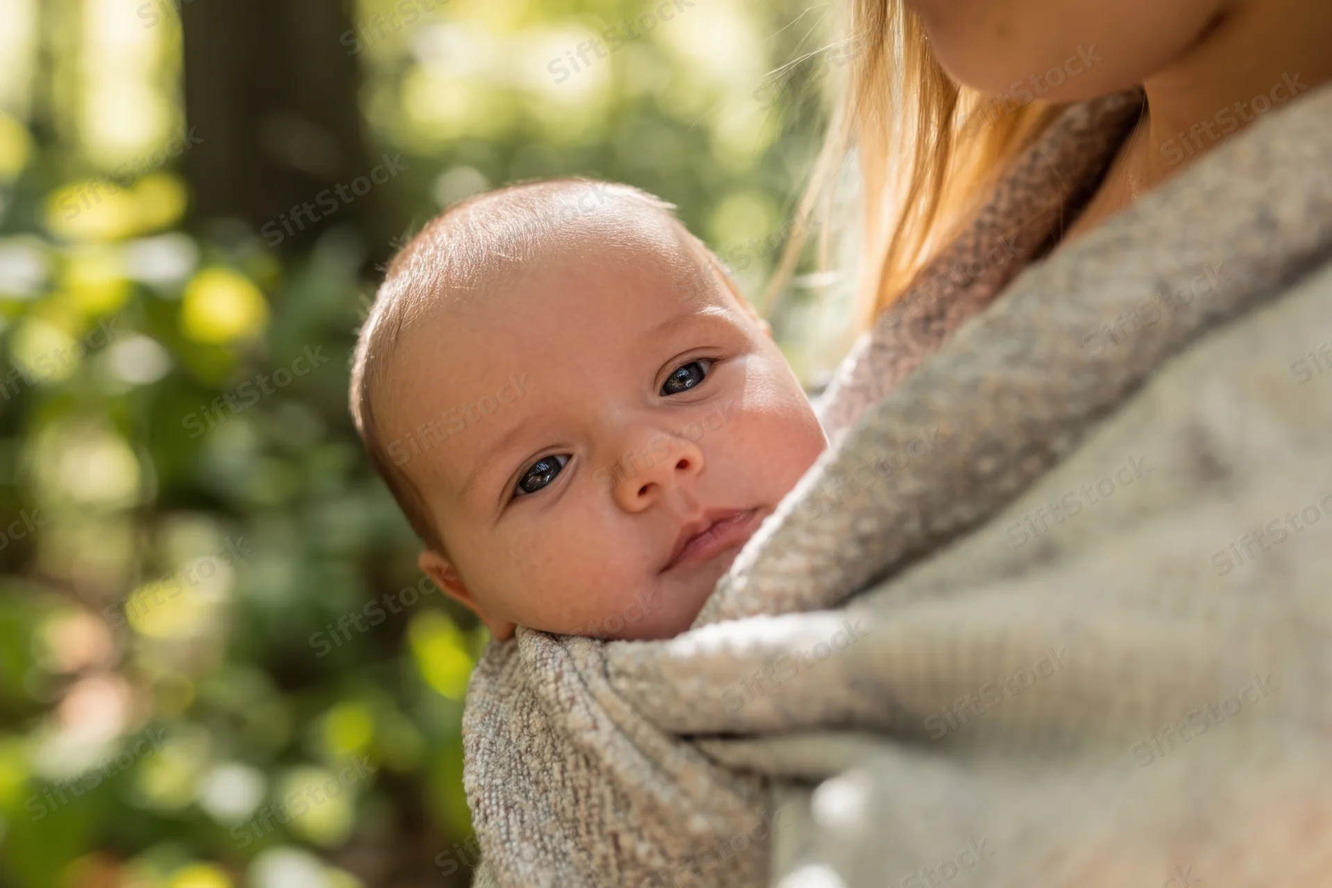 Baby wrapped in textured fabric sling held by mother outdoors