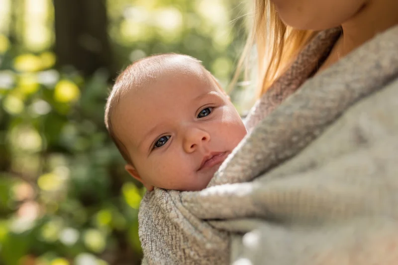 Baby wrapped in textured fabric sling held by mother outdoors