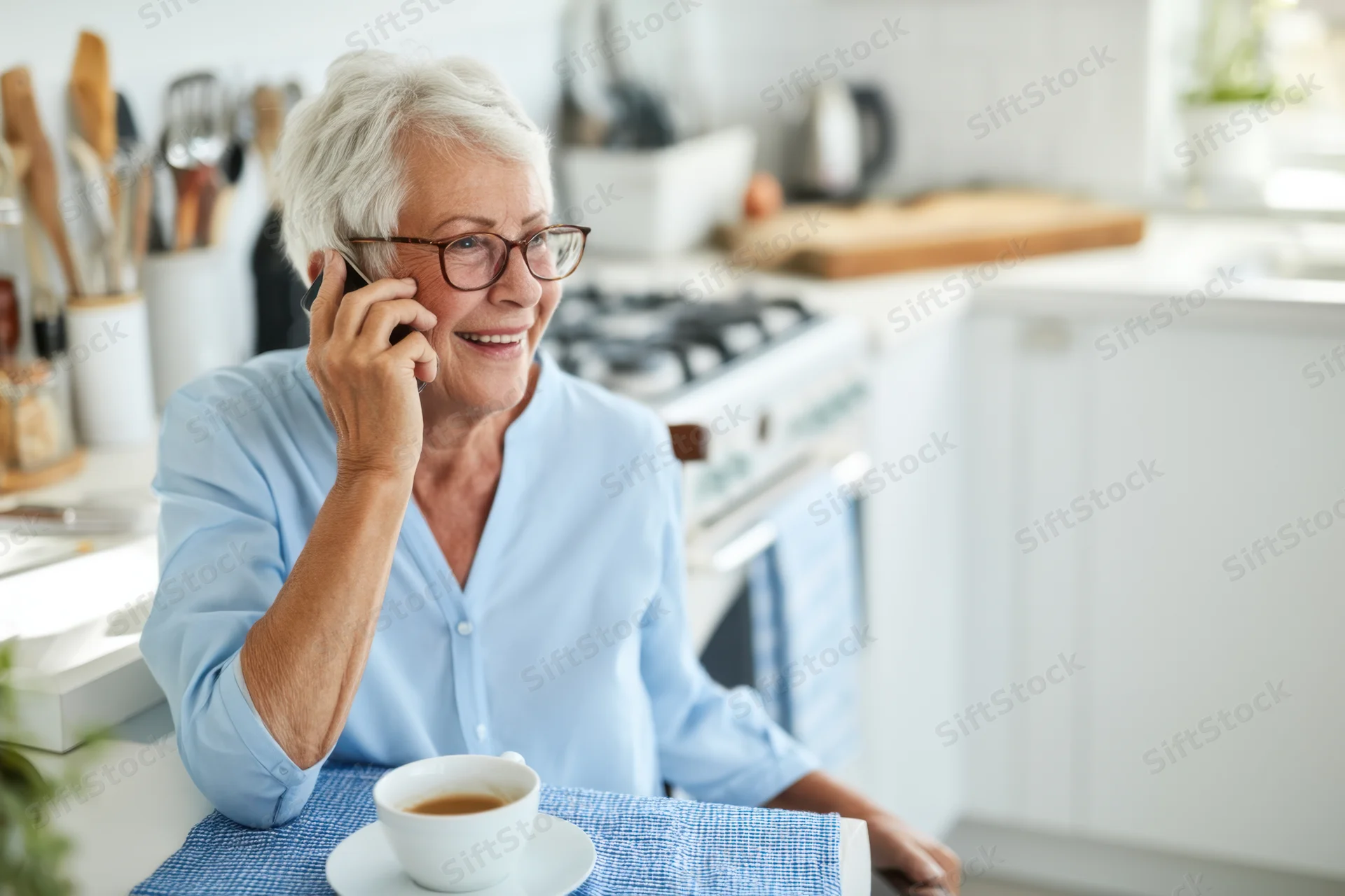 Senior woman smiling while talking on phone in kitchen with tea cup on table