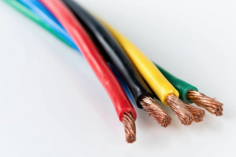 Multicolored electrical wires with plastic insulation and exposed copper strands arranged diagonally on white background