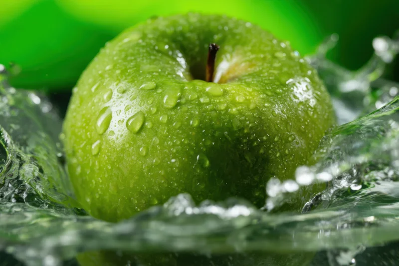 Green apple with water droplets and splash in closeup view