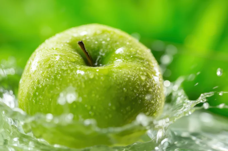 Green apple with water droplets splashing around it on a blurred green background