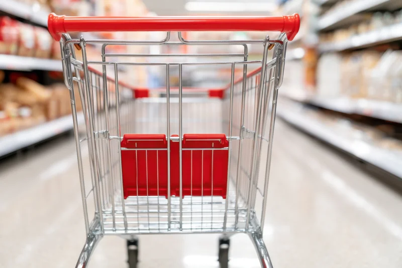 Shopping cart with chrome frame and red handle in supermarket aisle