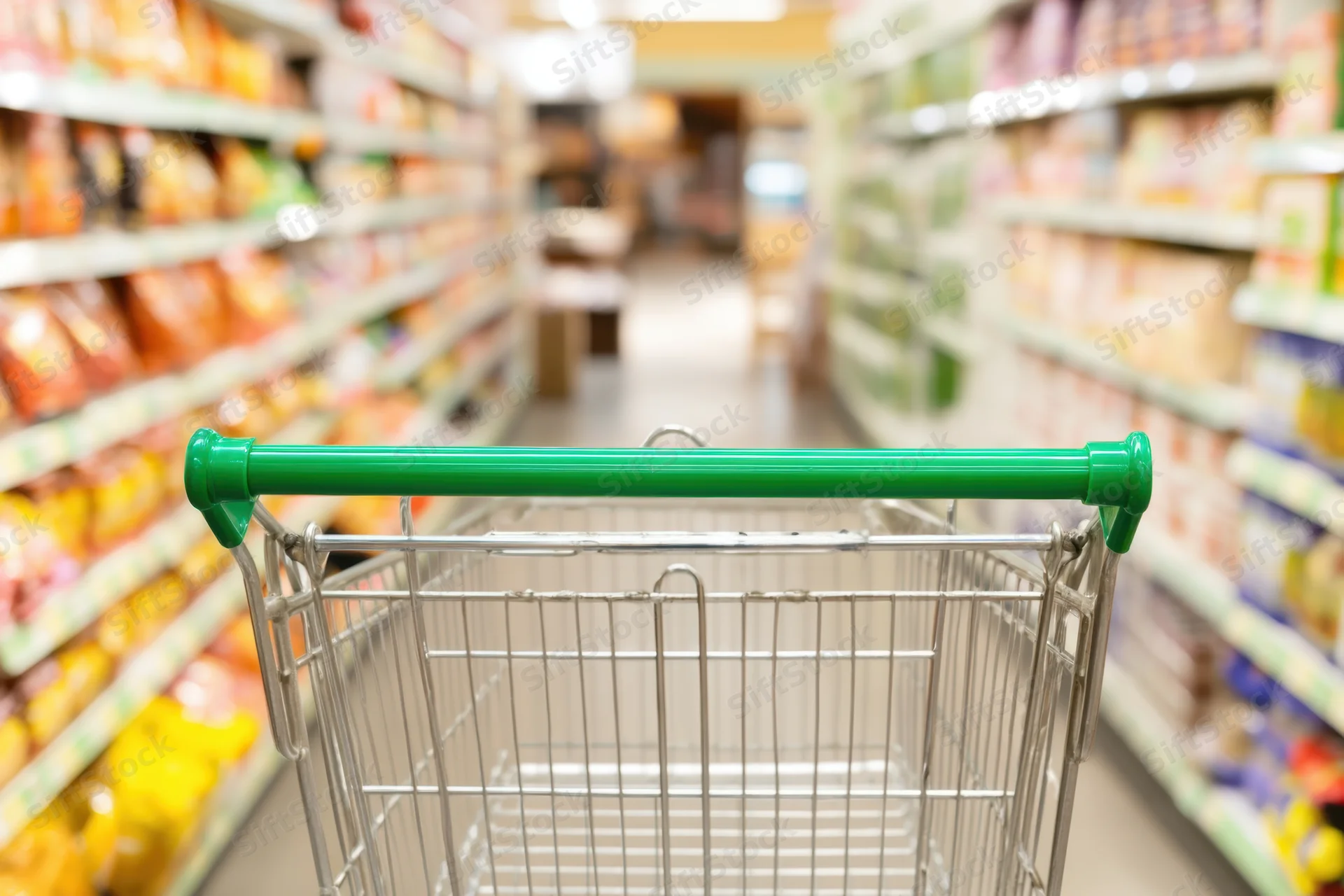 Shopping cart in foreground facing down supermarket aisle with shelves of products on both sides