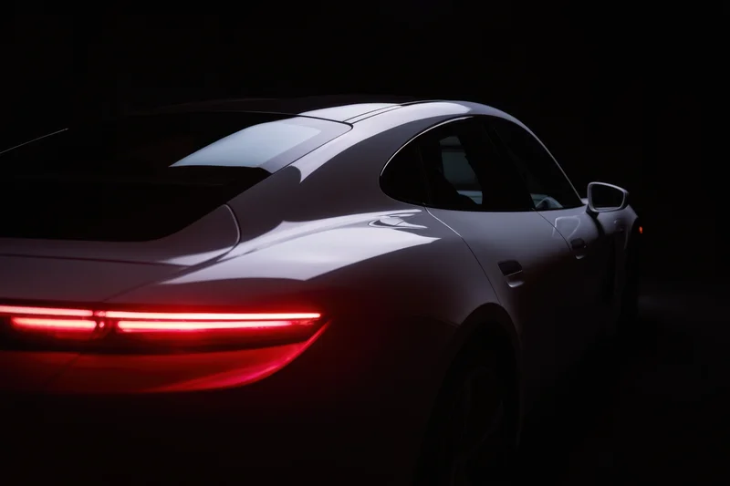 Sleek white electric car shown from rear side profile in dark studio lighting with glowing red taillight