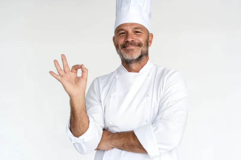 Smiling male chef in white uniform making ok gesture with arms crossed in studio