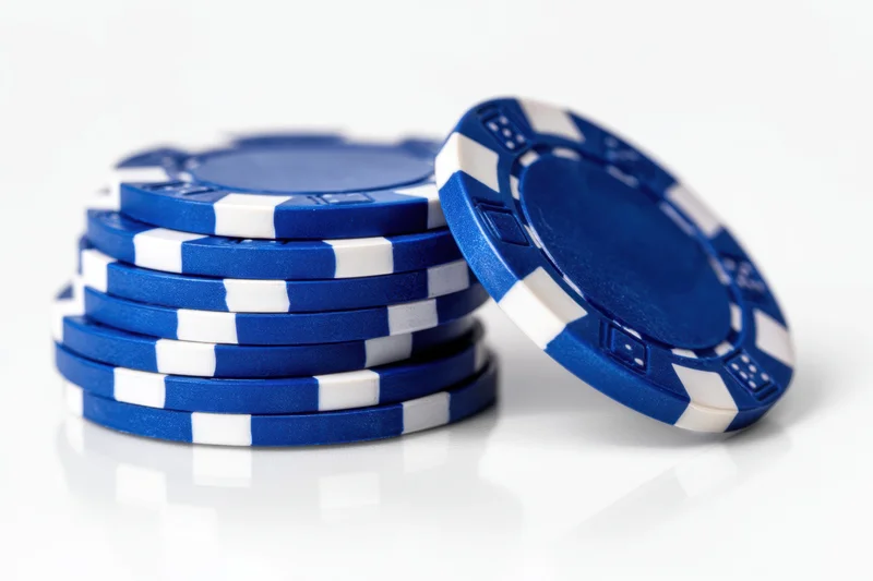 Stack of blue poker chips with white stripes on reflective white surface