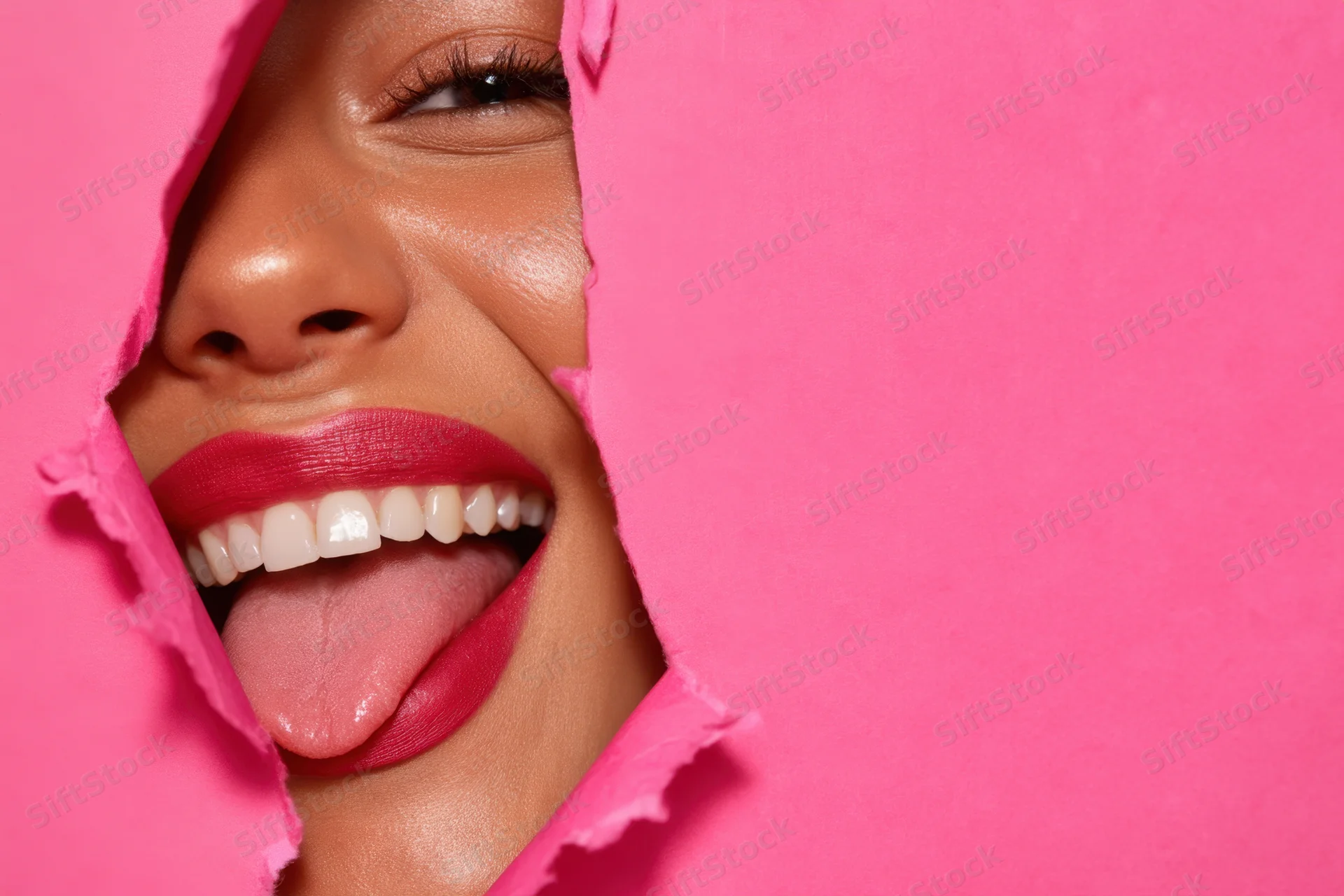 Woman smiling with tongue out through tear in pink paper