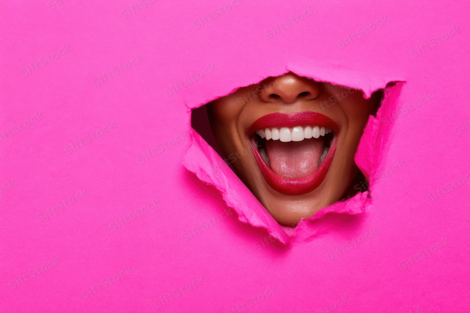 Woman’s laughing mouth visible through a torn pink paper hole