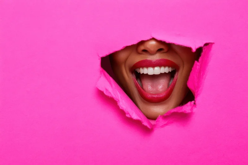 Woman’s laughing mouth visible through a torn pink paper hole