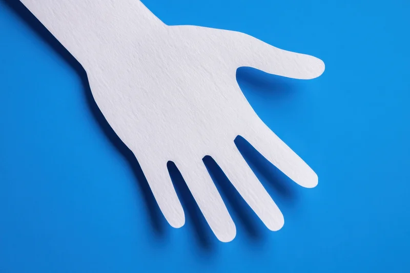 White paper hand cutout lying flat on vibrant blue background