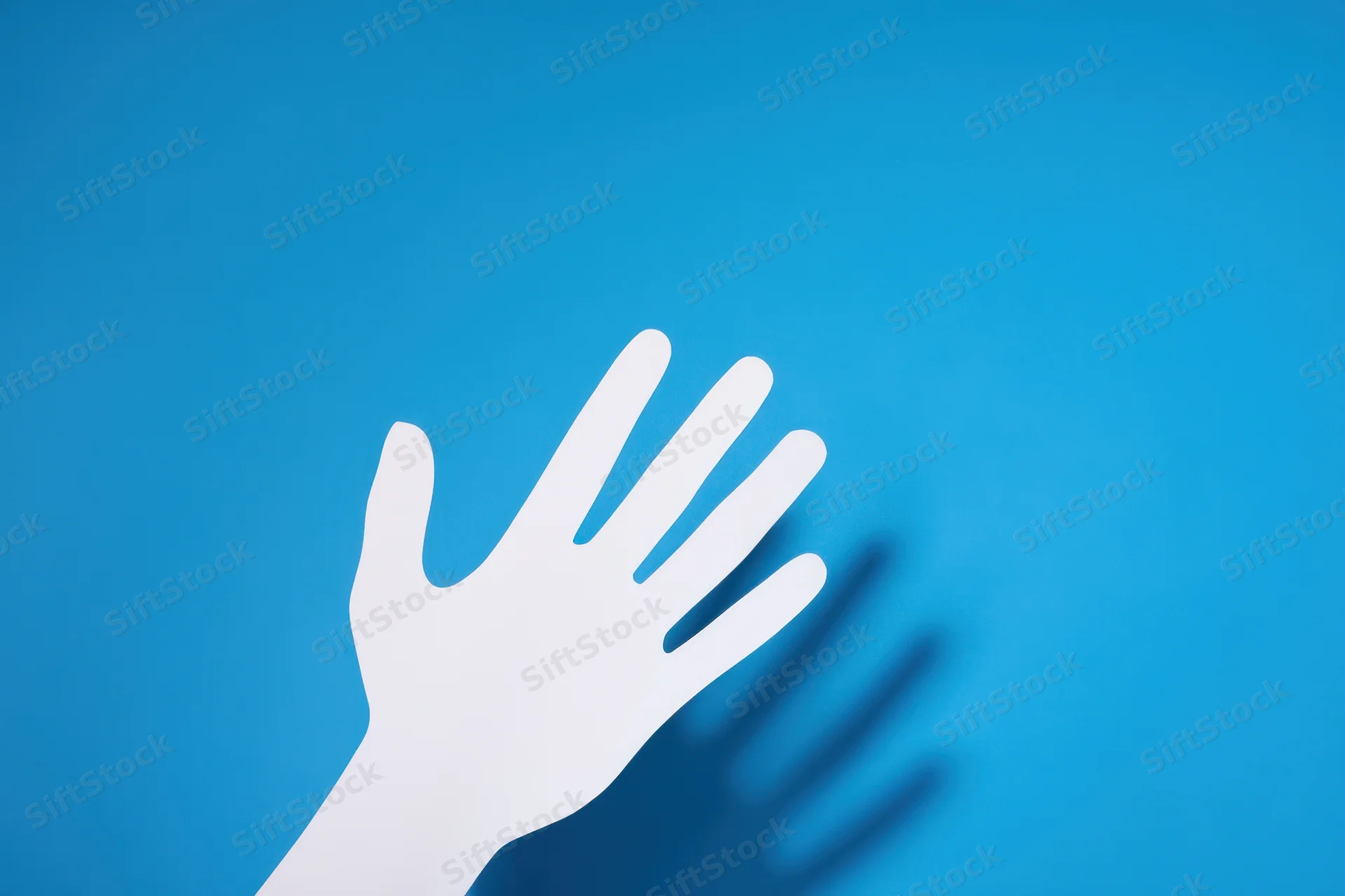 White paper cutout of a hand with shadow on blue background