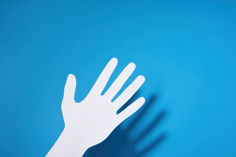 White paper cutout of a hand with shadow on blue background