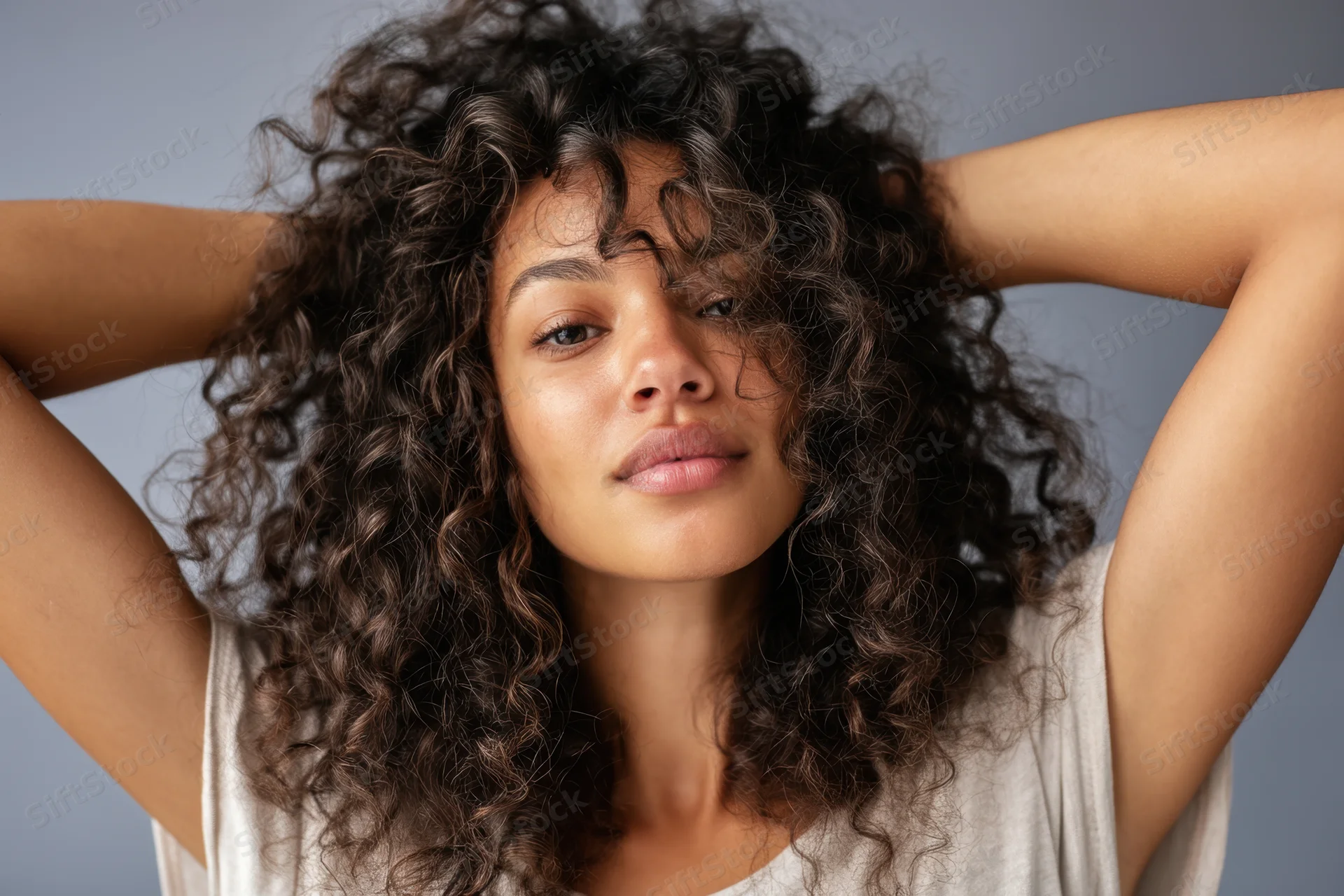 Young black woman with curly hair holding hands behind head in studio portrait