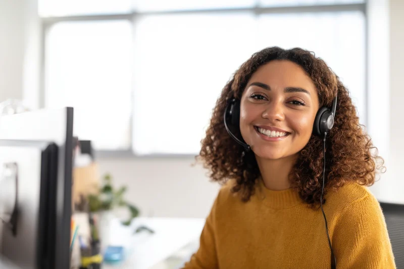 Woman wearing headset smiling at camera in office workspace