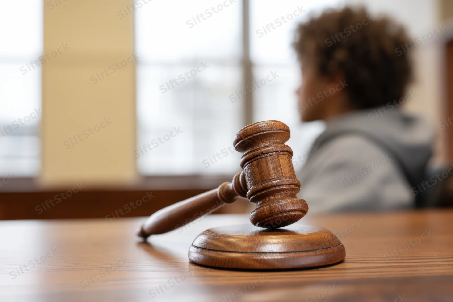 Wooden gavel resting on sound block in courtroom with judge in background