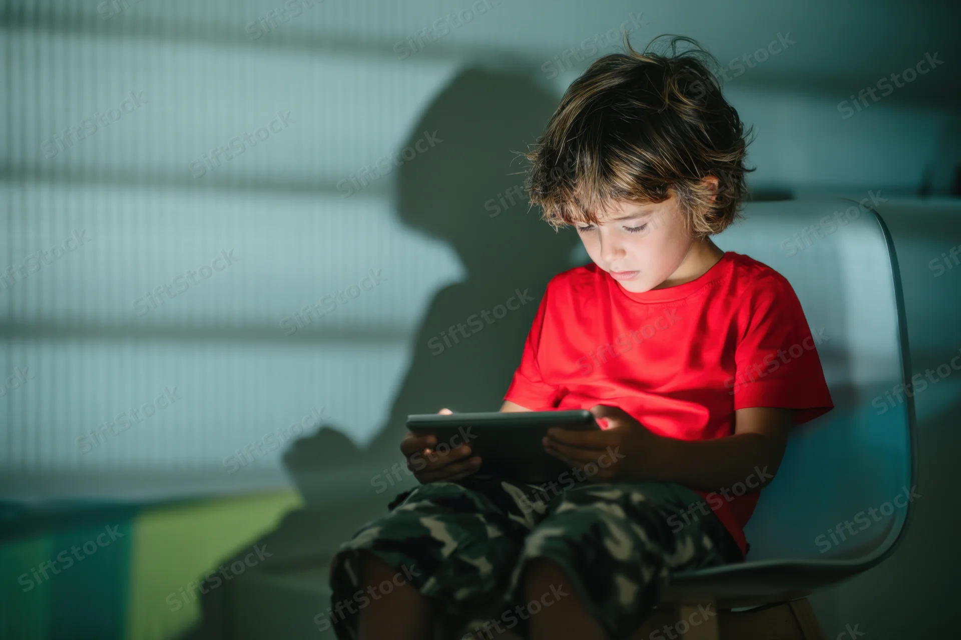 Young boy sitting on a modern chair concentrating on a tablet screen indoors