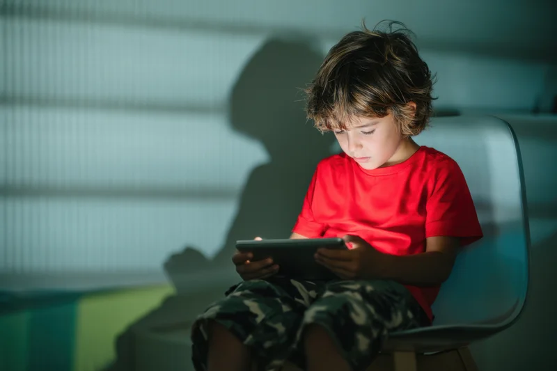 Young boy sitting on a modern chair concentrating on a tablet screen indoors