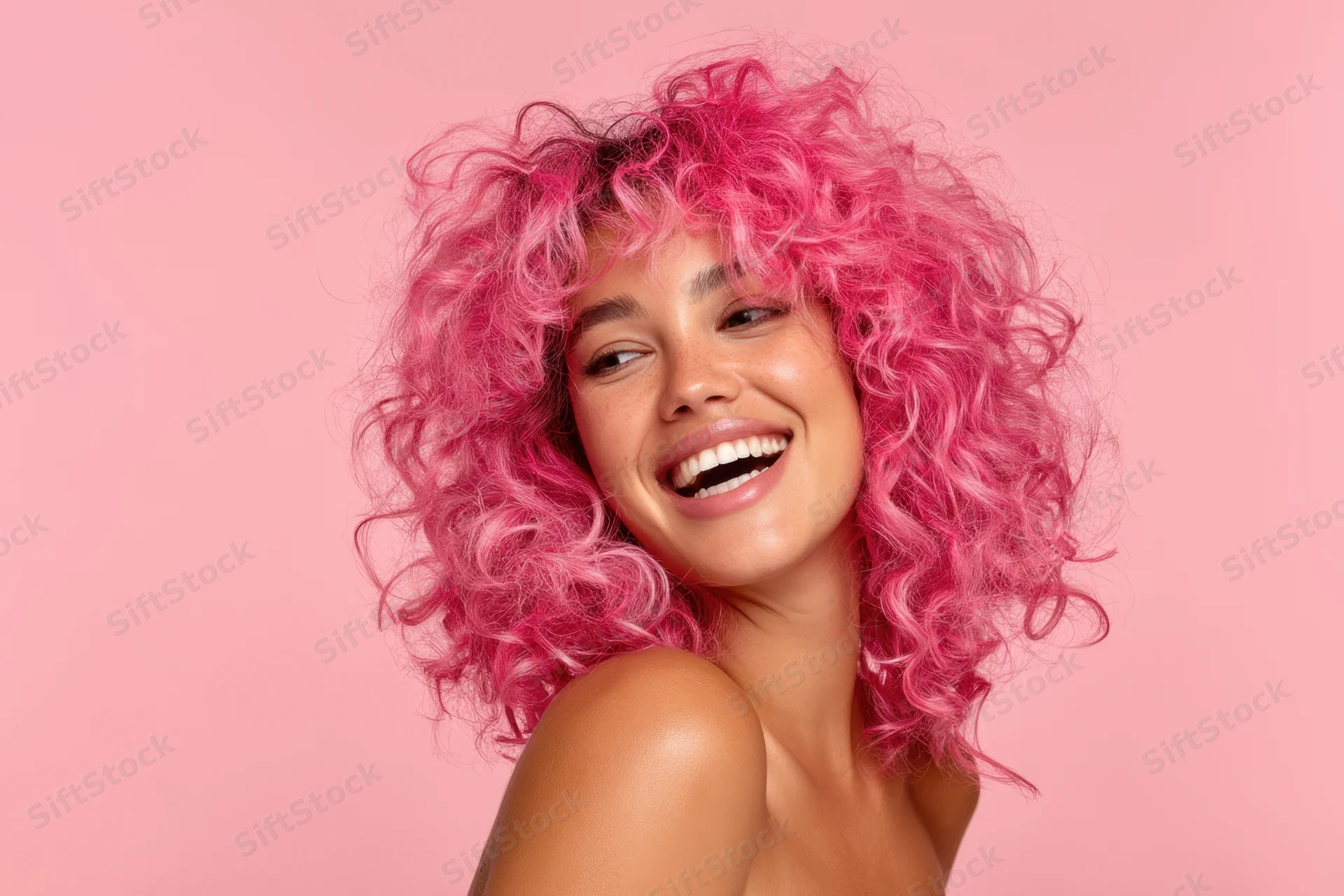 Young woman with vibrant pink voluminous curly hair laughing in studio portrait