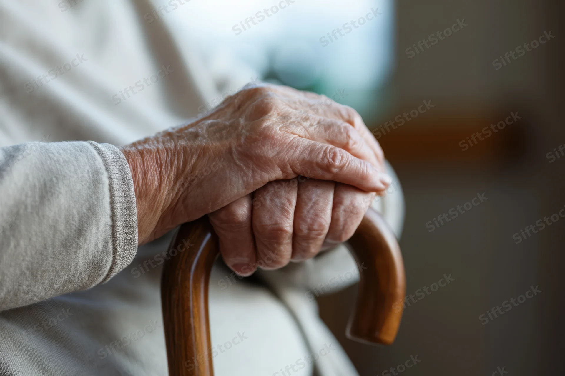 Elderly hands clasped around a wooden cane for support indoors