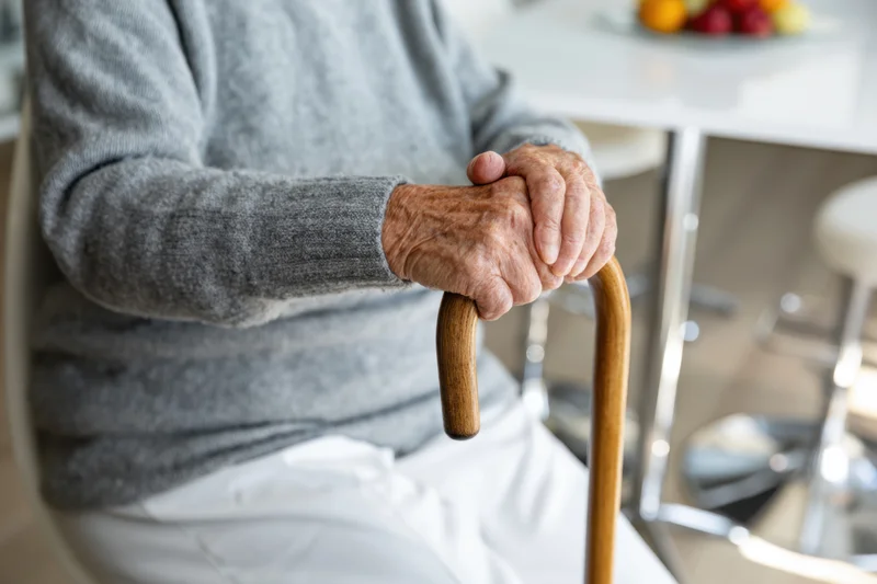 Senior woman gripping wooden cane while seated in kitchen interior