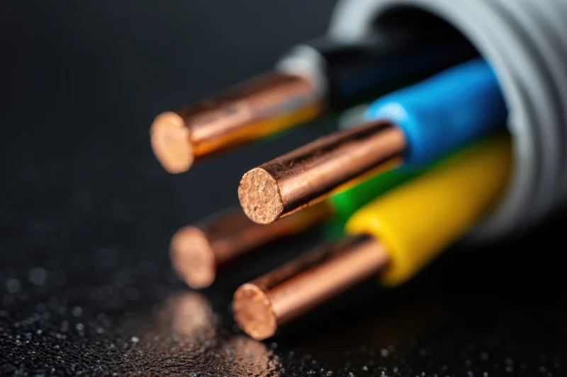 Copper electrical wires emerging from a grey flexible conduit on dark surface
