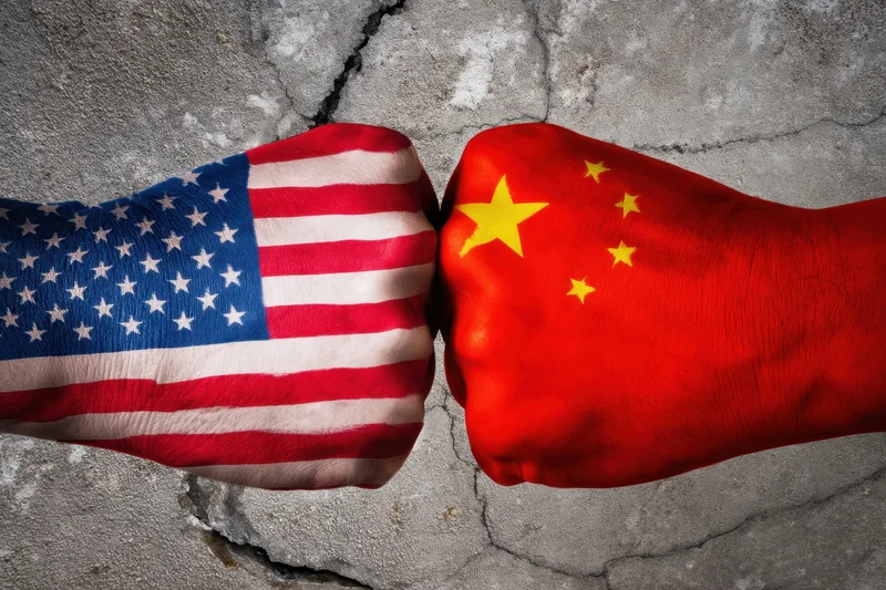 Two fists painted with american and chinese flags colliding against cracked concrete wall