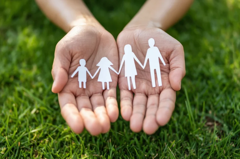 Hands holding paper cutout family figures over green grass