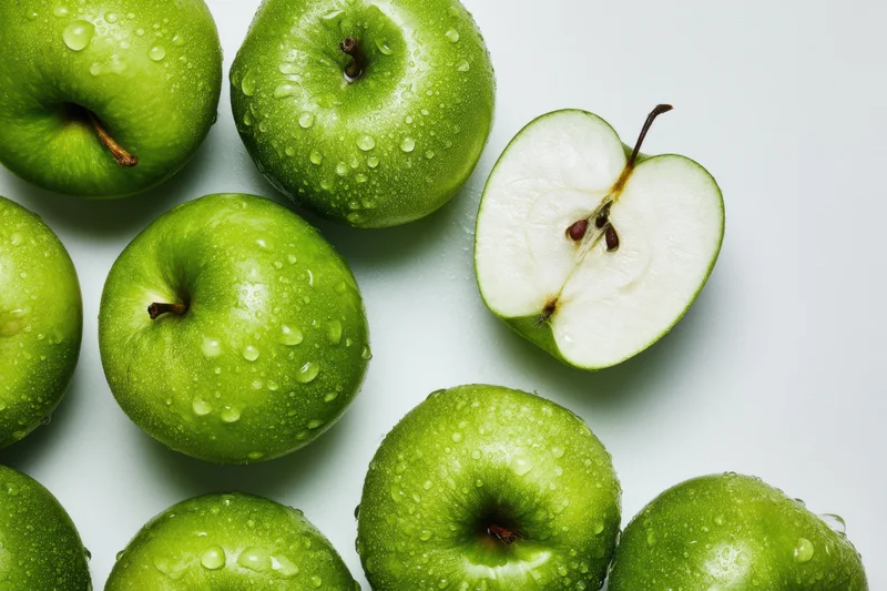 Green apples whole and sliced with water droplets on white surface