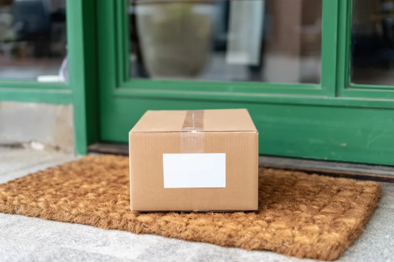 Cardboard box with blank label placed on doormat at front door entrance