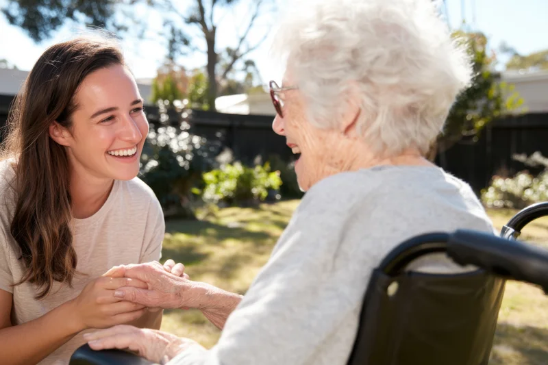 Caregiver holding hands with smiling senior woman in wheelchair outdoors in garden