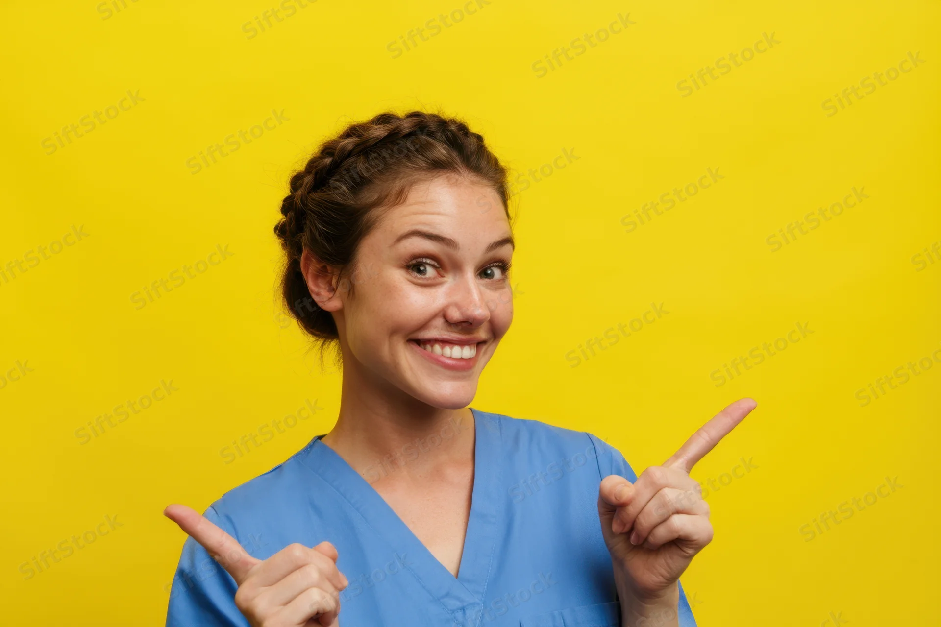 Woman in blue scrubs pointing with smile against yellow background