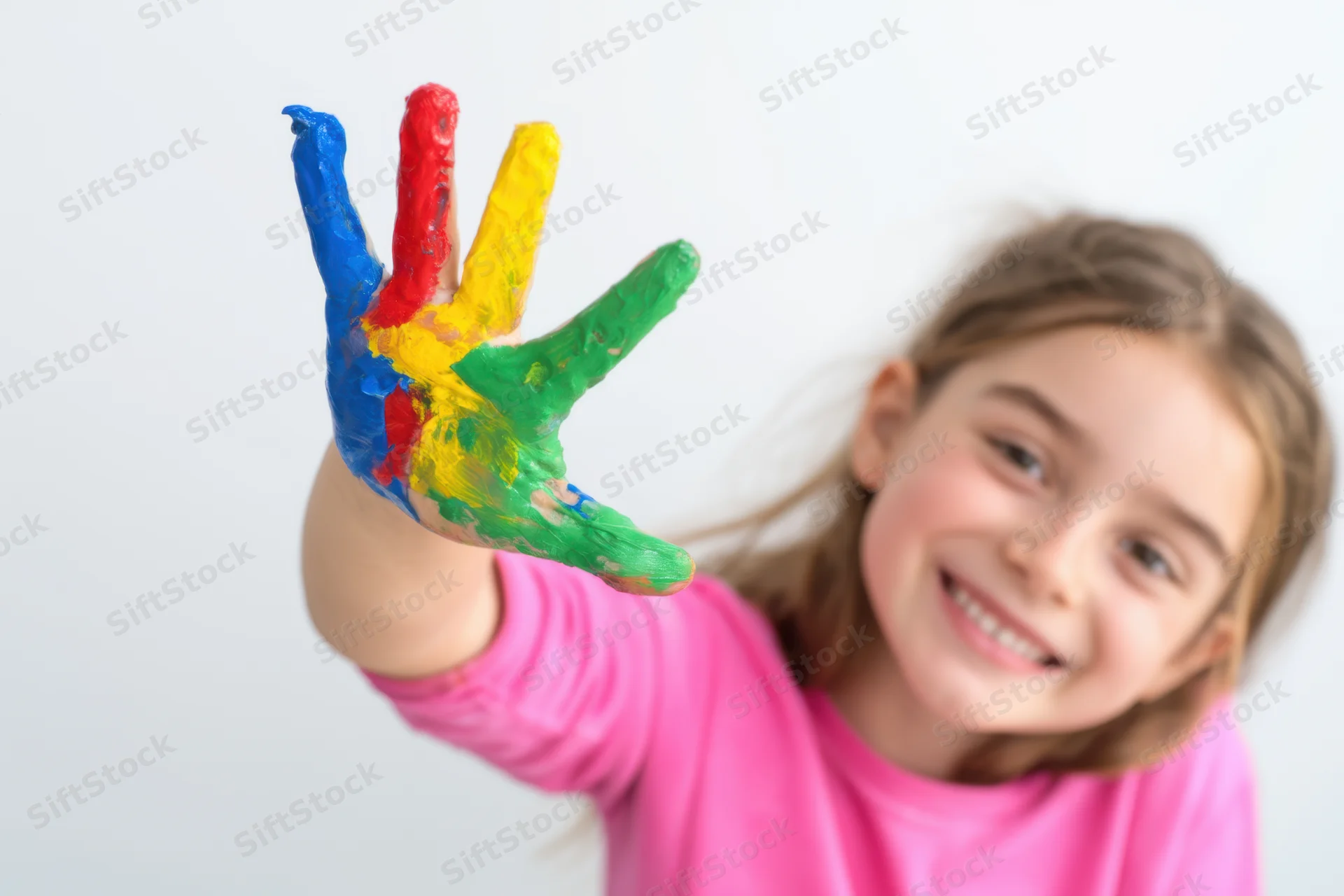 Young girl smiling with paint-covered hand extended toward camera in pink shirt