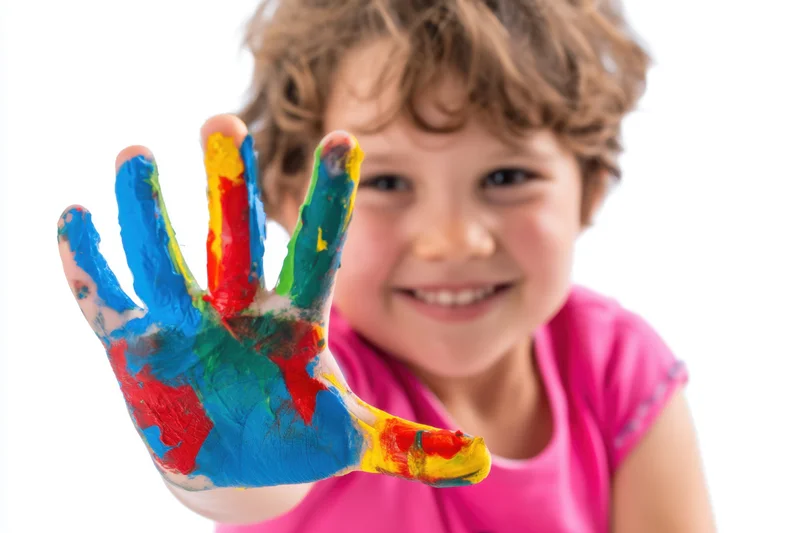 Child holding out paint-covered hand toward camera in studio setting