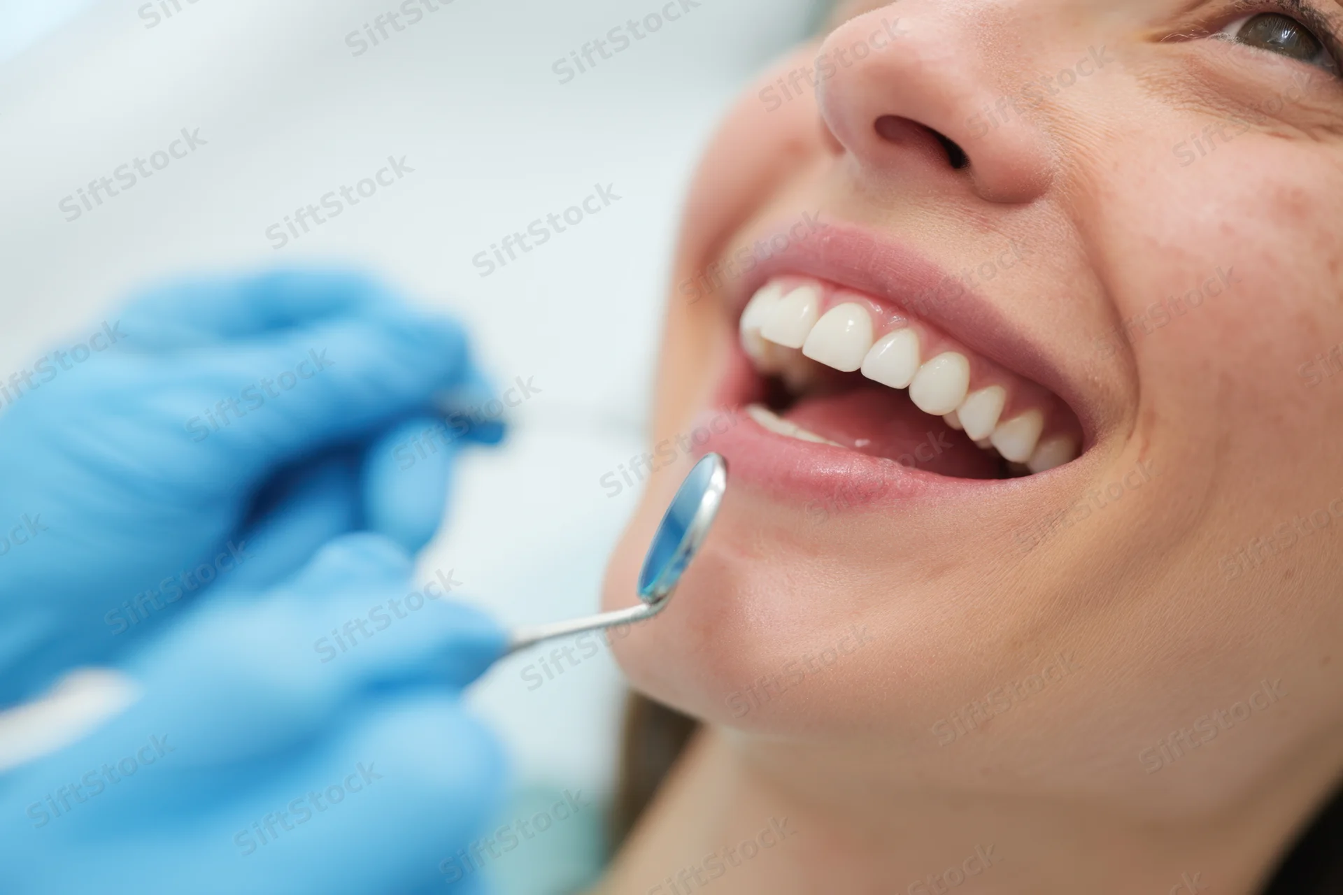 Woman smiling during dental examination with dentist using mirror in clinic