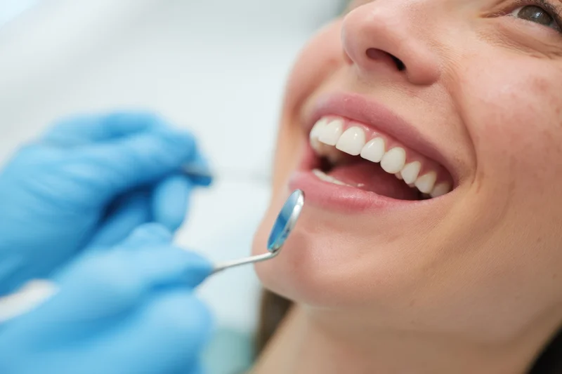 Woman smiling during dental examination with dentist using mirror in clinic