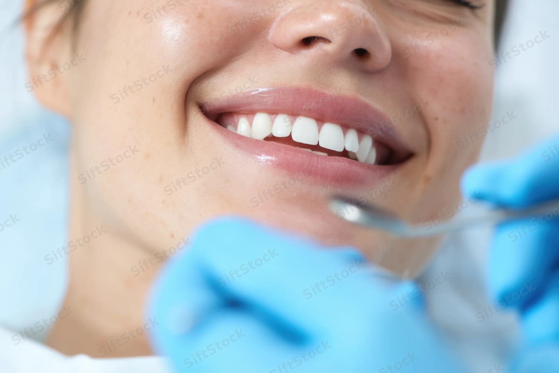 Woman smiling during dental examination with dentist using mirror and blue gloves