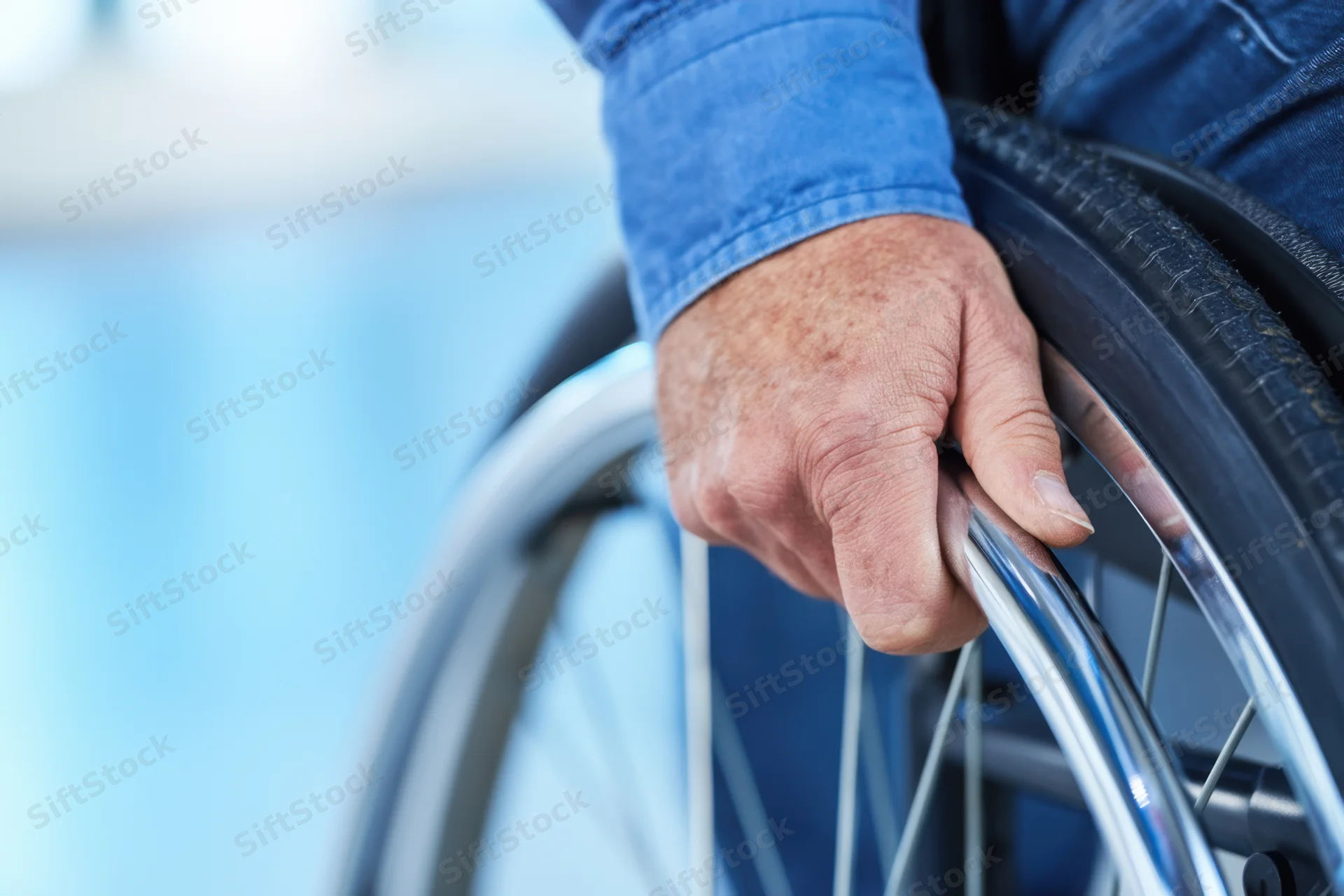 Close-up of a man's hand gripping the wheel of a wheelchair, showing mobility aid in use
